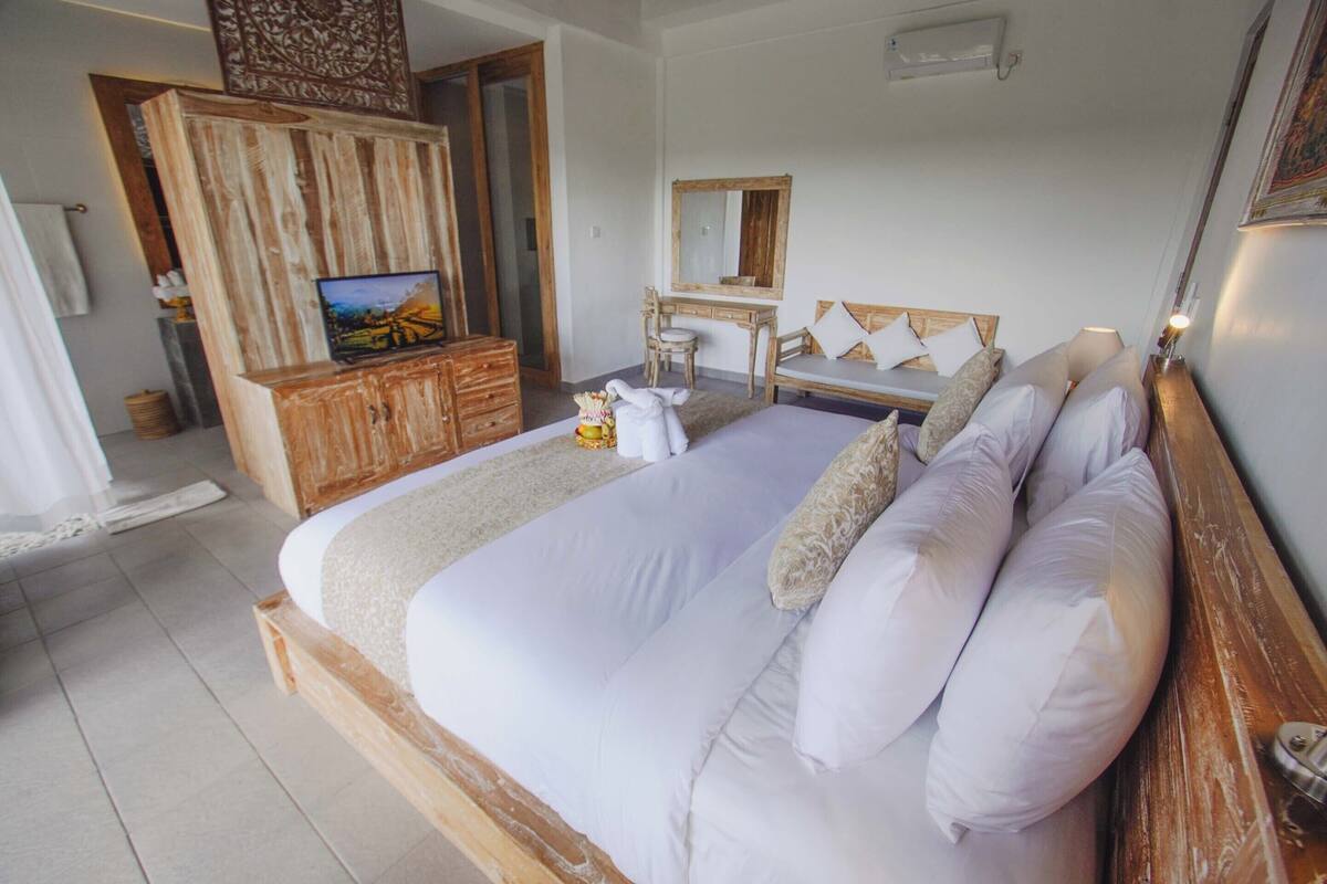 Un dormitorio con una cama grande, un aparador de madera, un tocador con espejo y un televisor sobre un mueble de madera.