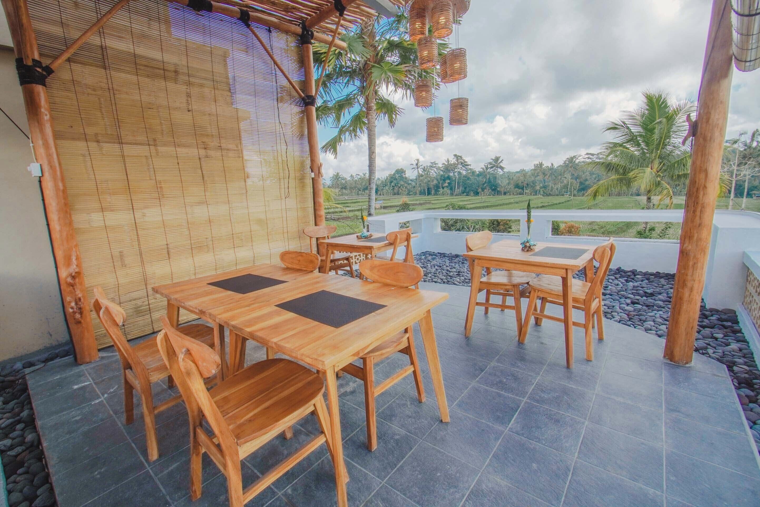 A wooden outdoor dining area with two tables and chairs, bamboo wall, and a view of a lush landscape.