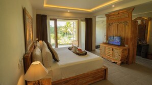A bedroom with a large bed, a wooden dresser, a television, and a view of the outdoors. - The Nenggala Suite (Taro)