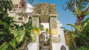 A stone gateway with intricate carvings, flanked by statues and lush tropical foliage. - The Nenggala Suite (Taro)