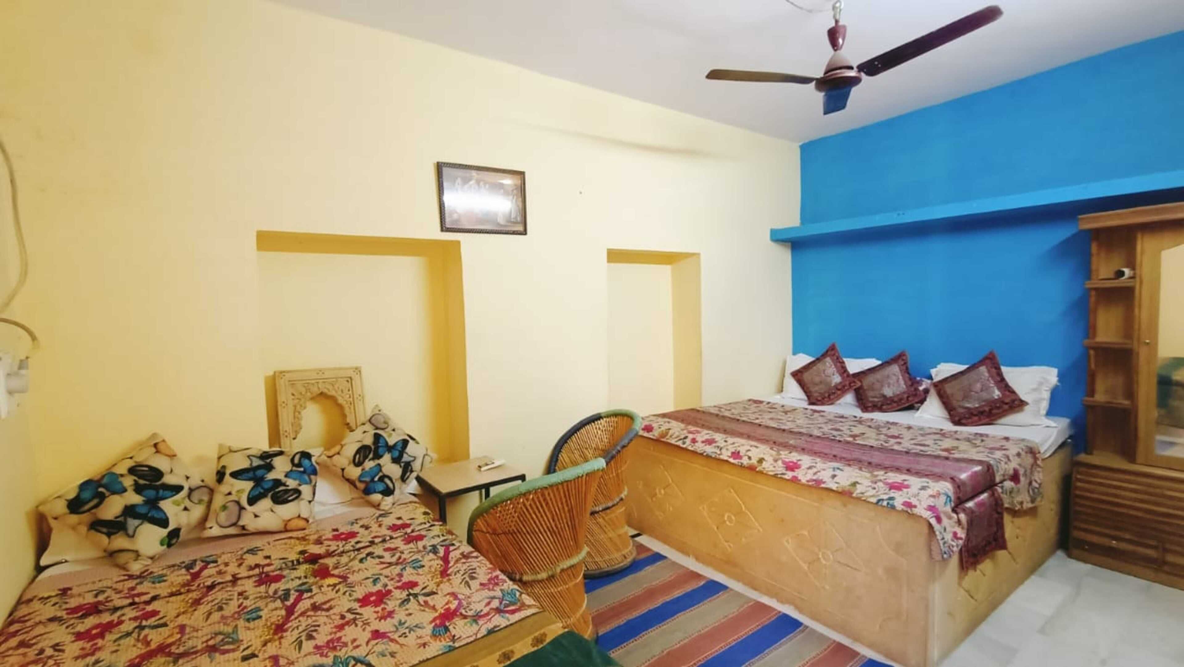 Habitación con dos camas, una silla, un ventilador de techo y un estante en la pared.