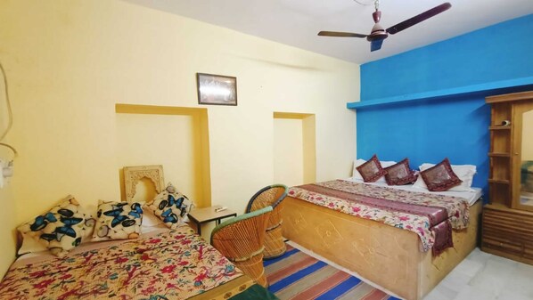 A room with two beds, a chair, a ceiling fan, and a wall-mounted shelf.
