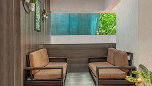 A room with two wooden sofas, a small rug, and a window with a blue curtain. - iROOMZ Eco Avasya Residency (Hyderabad)