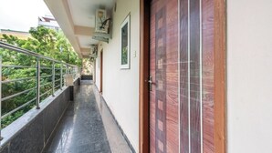 A corridor with a metal railing, a wooden door, and a wall-mounted air conditioning unit. - iROOMZ Eco Avasya Residency (Hyderabad)
