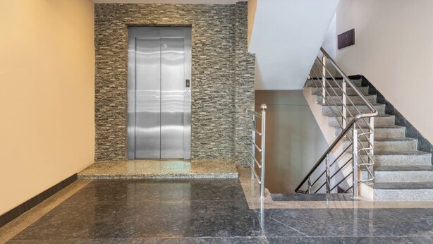 A modern elevator with a stone facade, a marble floor, and a staircase with metal railings. - iROOMZ Eco Avasya Residency (Hyderabad)