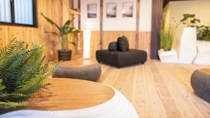 Un interior moderno con suelo de madera, una mesa redonda de madera, un sofá negro y plantas en macetas.
