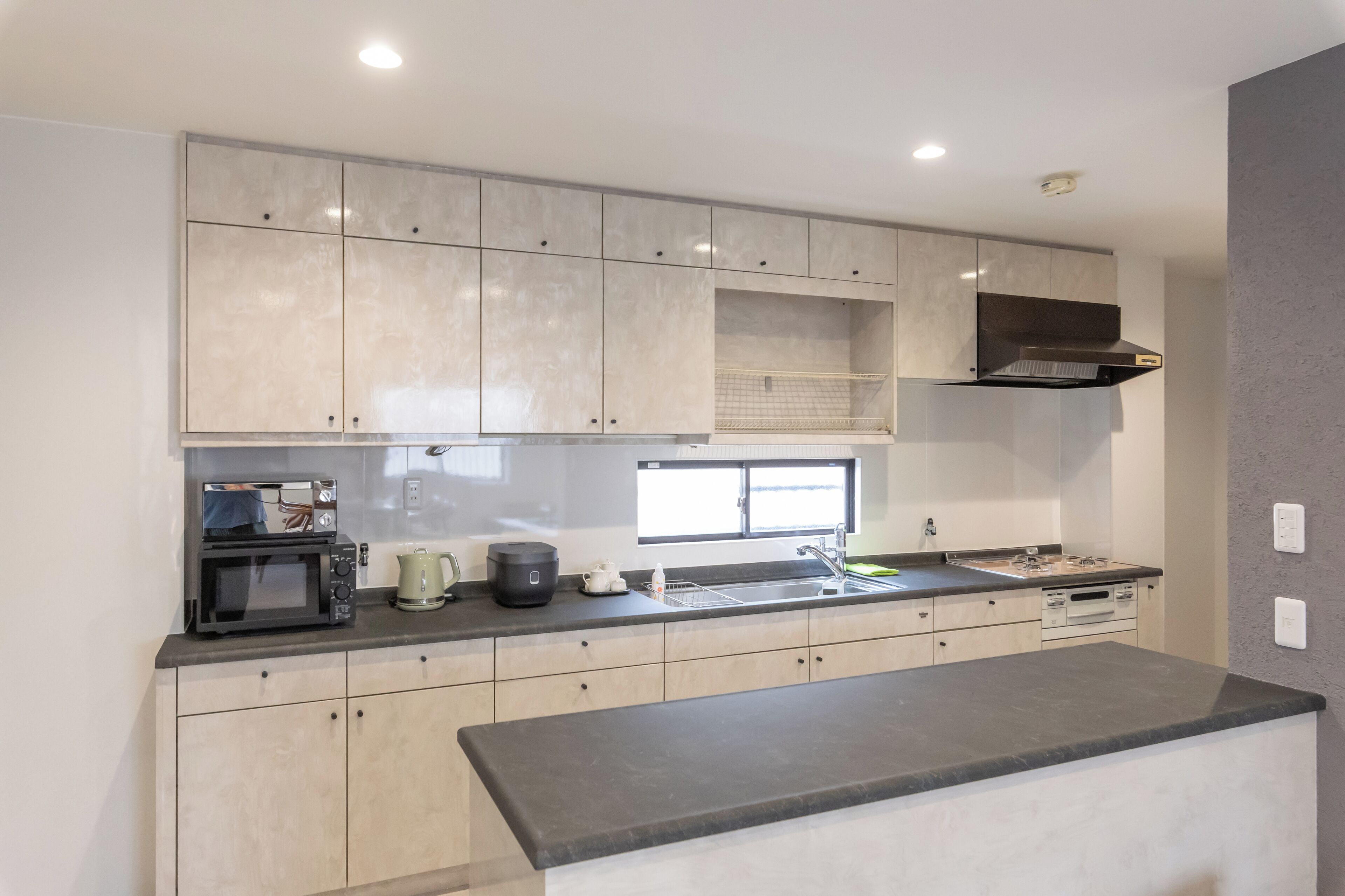A modern kitchen with light-colored cabinets, a built-in microwave, a kettle, and a sink.