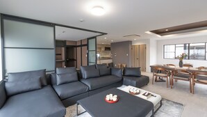 Una sala de estar moderna con un sofá modular, una mesa de centro con adornos y un comedor con sillas de madera y una mesa.