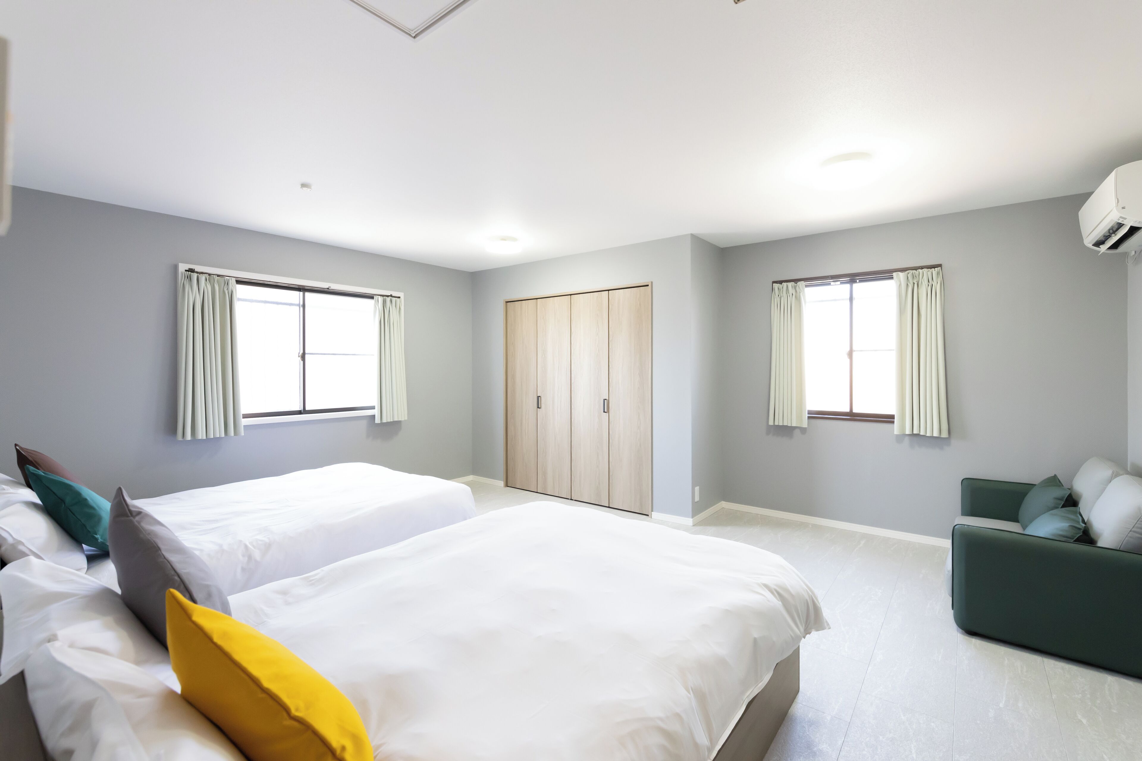 Una habitación de hotel moderna con dos camas, un sofá verde y un armario.