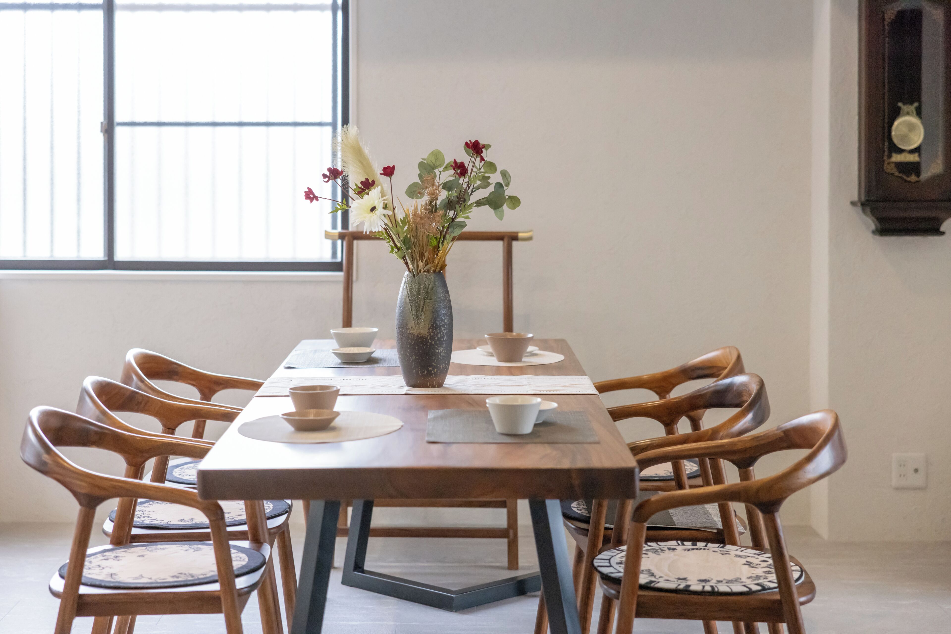 Una mesa de comedor con seis sillas de madera, un jarrón con flores y un reloj de pared.