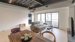 Un espacio de estar moderno con una mesa de comedor de madera, un sofá gris y un televisor.