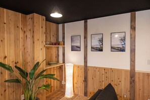A room with wooden panel walls, a floor lamp, a plant, and three framed pictures on the wall. - TOYOTSUKI (Osaka)