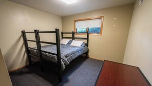 Eenpersoonskamer met een stapelbed, vloerbedekking, een raam met zonwering en een klein houten tafeltje.