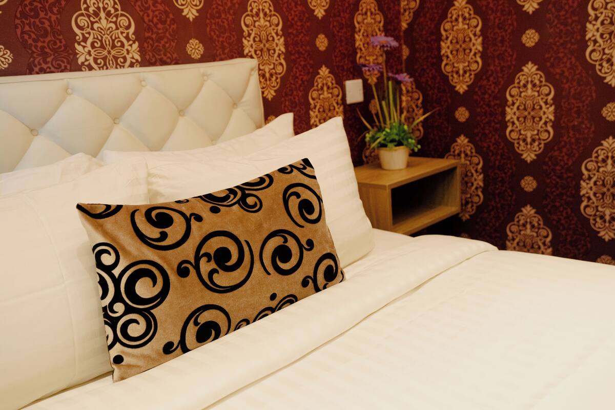 A neatly made bed with a patterned pillow, a tufted headboard, and a small wooden nightstand with a potted plant.
