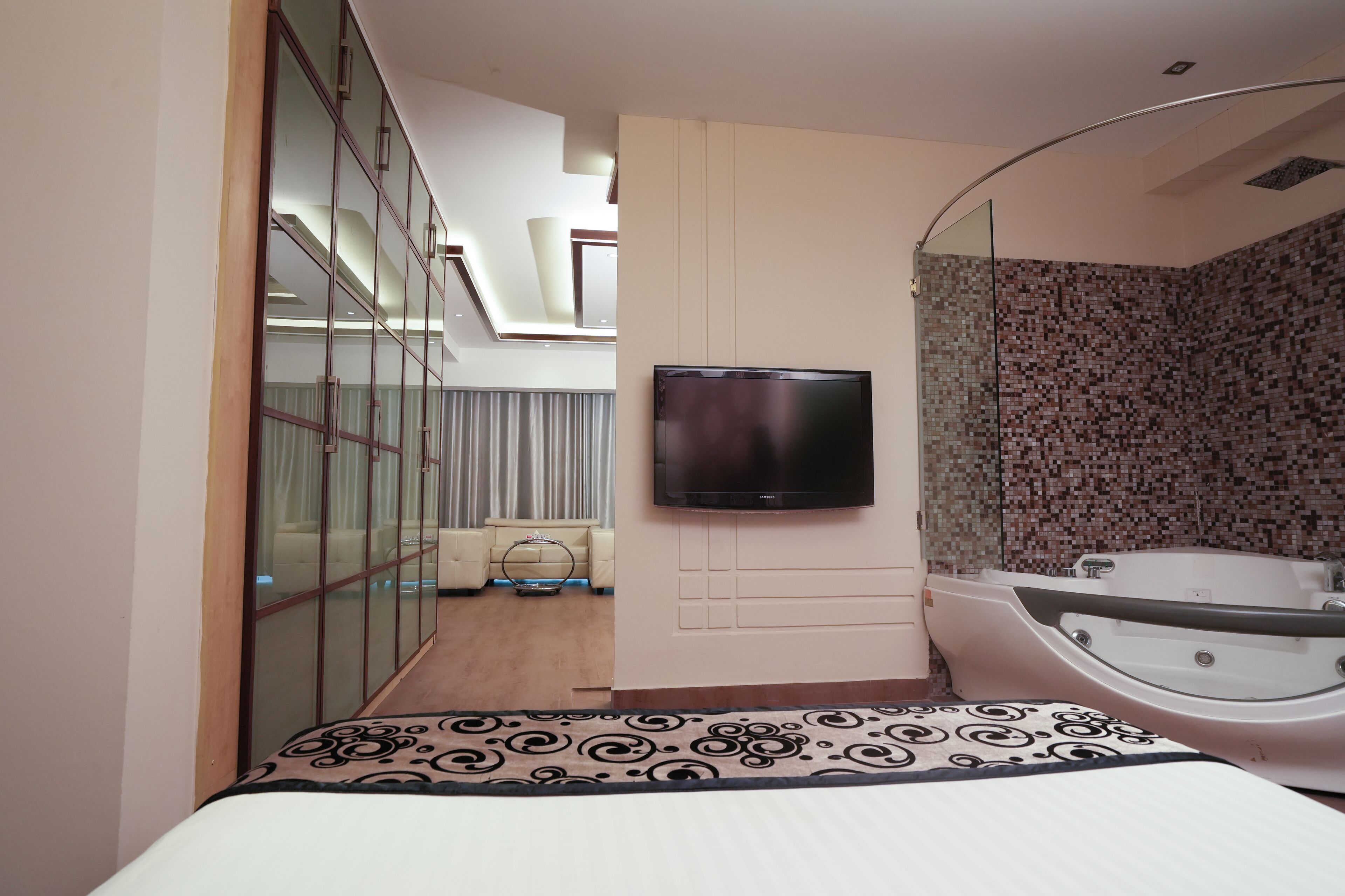 Een moderne hotelkamer met een groot bed, een aan de muur bevestigde televisie, een aparte badkamer met een badkuip, en een glazen wand die de kamer van de gang scheidt.