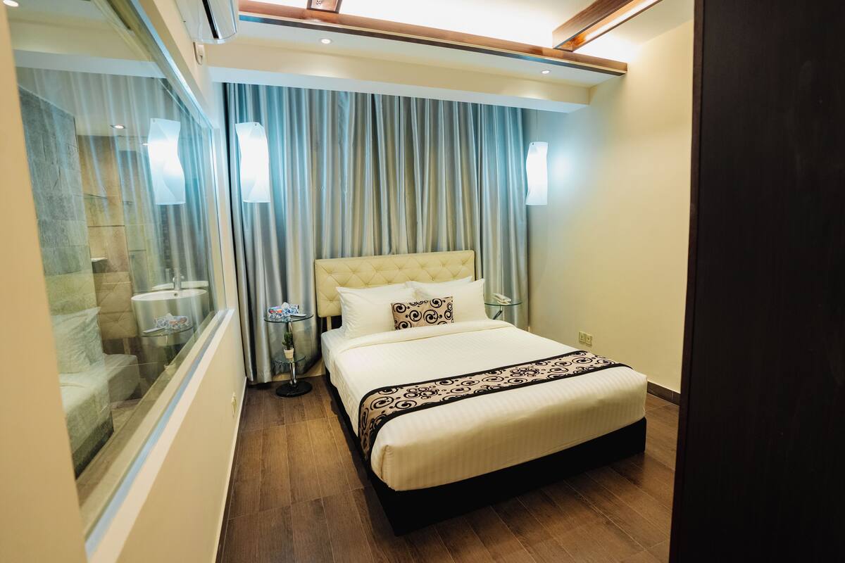 A hotel room with a bed, curtains, bedside tables, and a glass partition.