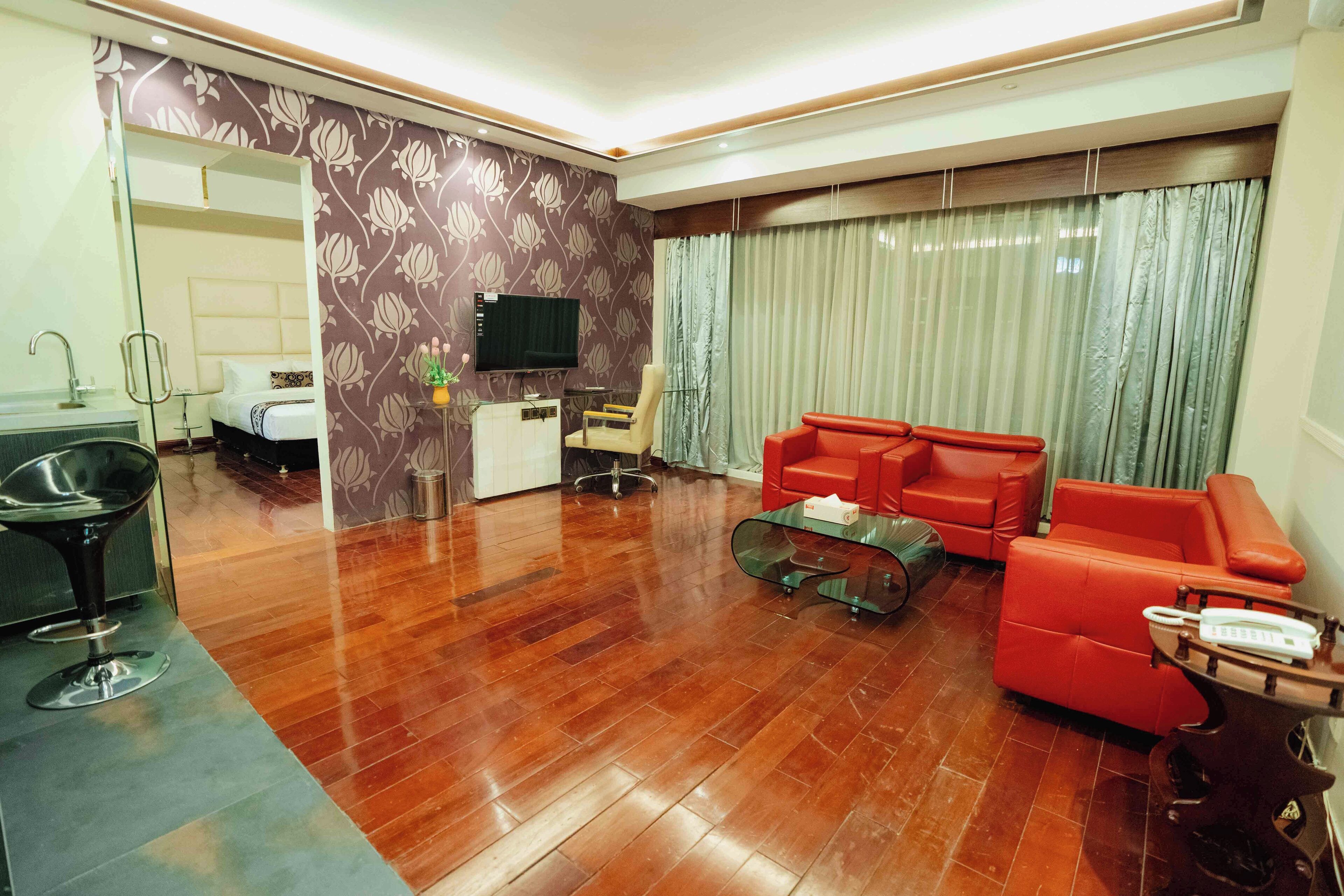 A modern living room with a wooden floor, a red sofa, a glass coffee table, and a TV on the wall.