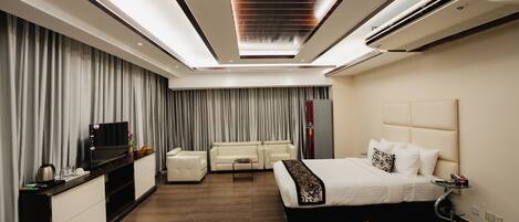 A modern hotel room with a large bed, a sofa, a TV, and a desk.