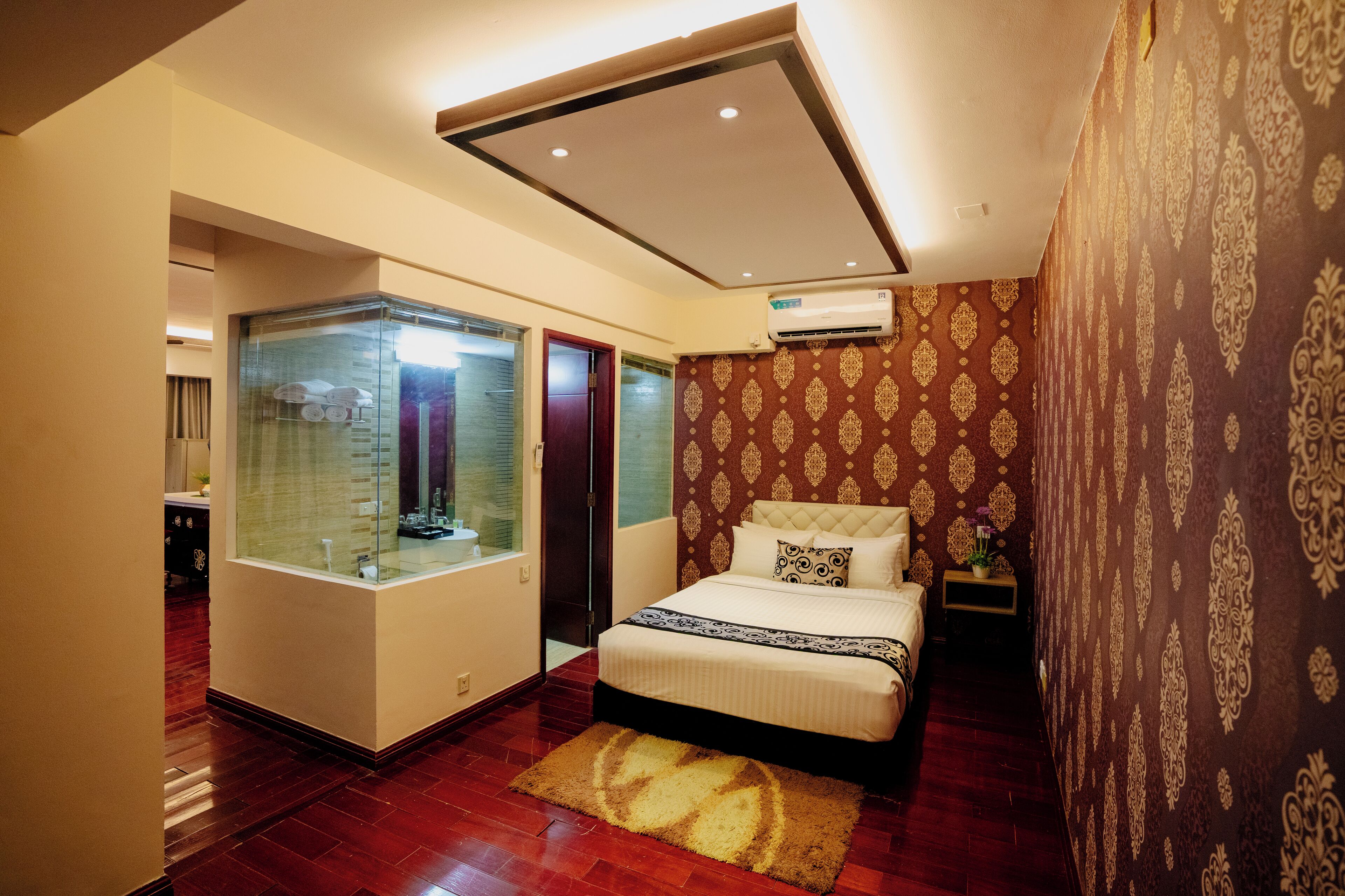 A bedroom with a large bed, a glass-enclosed bathroom, and patterned wallpaper.