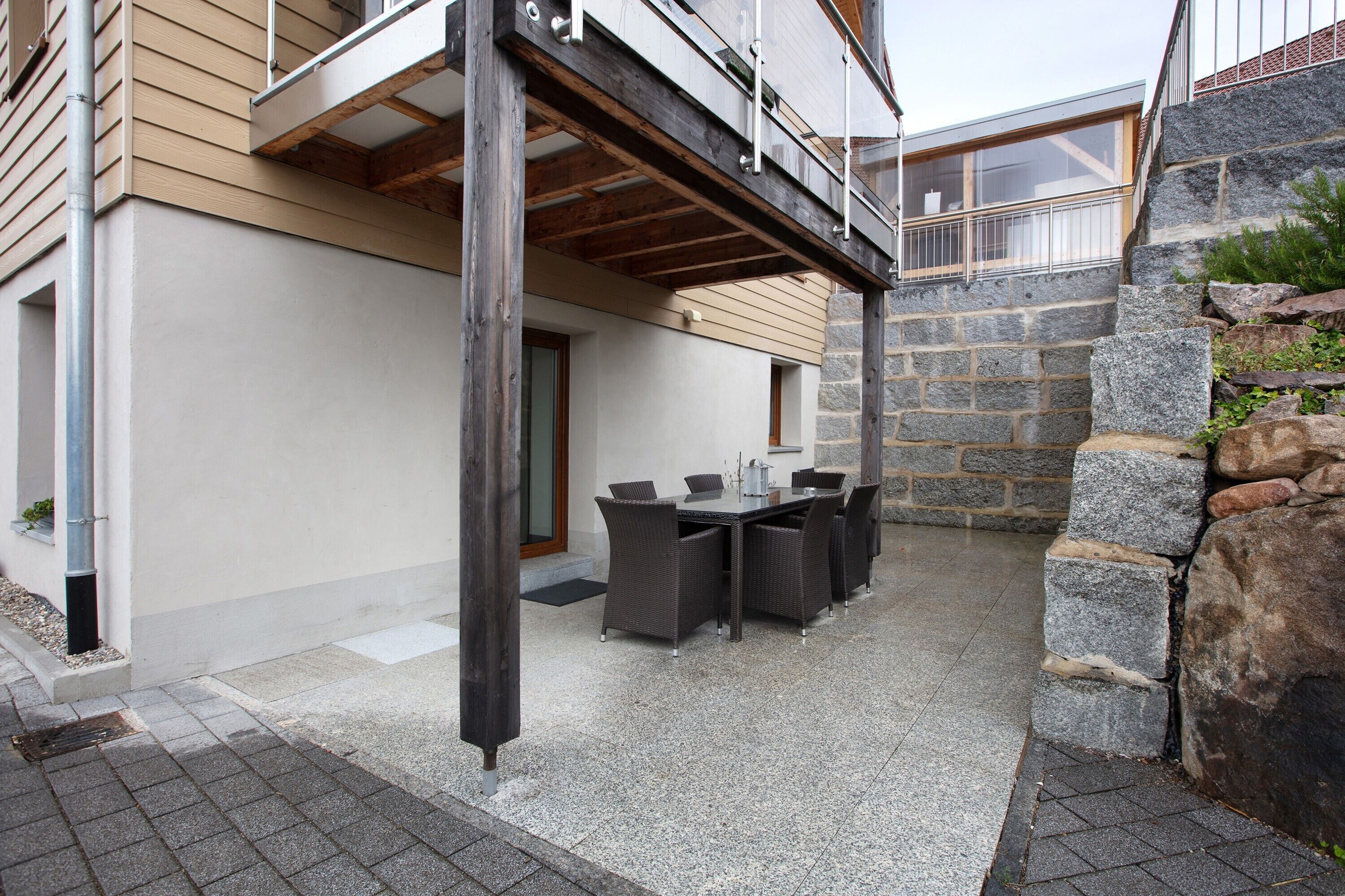 A covered outdoor patio with a table and chairs, stone walls, and a wooden beam structure.