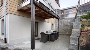 Un patio techado al aire libre con una mesa y sillas, paredes de piedra y estructura de vigas de madera.
