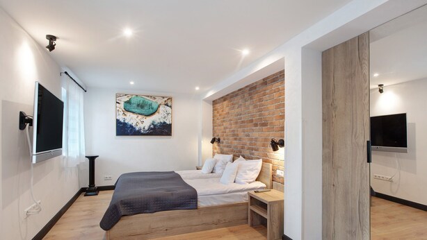 Un dormitorio moderno con una cama, un muro de ladrillo decorativo, un televisor montado y suelo de madera.