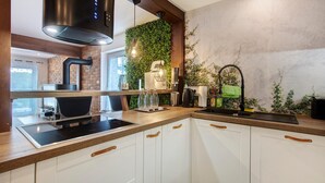 Una cocina con armarios blancos, extractor de acero inoxidable, pileta negra y pared verde con plantas.