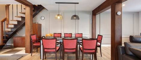Un comedor con una mesa y sillas de madera, una escalera y una sala de estar con sofá.