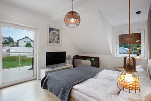 Une chambre à coucher comprenant un lit, une télévision, une table de chevet, une fenêtre avec des stores et une vue sur l’extérieur.