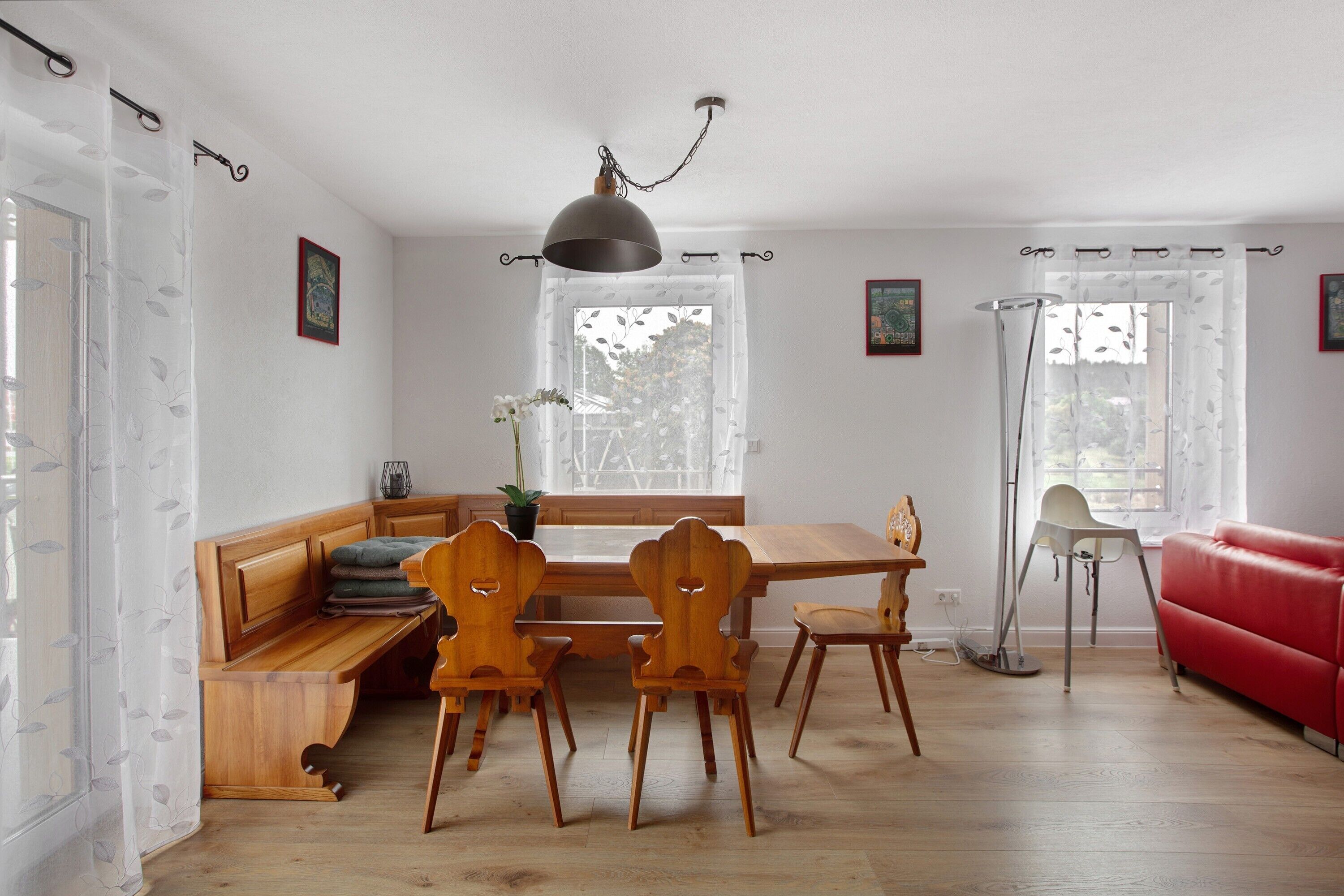 Zona pranzo con tavolo e sedie in legno, una panca, un divano rosso e una lampada da terra.