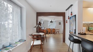 A modern kitchen with wooden flooring, a dining area with a round table and chairs, and a window with magazines.