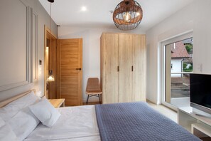 Une chambre à coucher comprenant un lit, une armoire, une chaise, un téléviseur et une grande fenêtre.