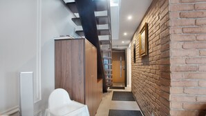 A narrow hallway with a wooden wardrobe, a white chair, a black mat, a brick wall, and a staircase.