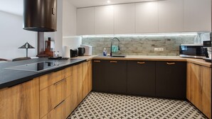 A modern kitchen with a black countertop, wooden cabinets, a stainless steel range hood, a tiled backsplash, and a microwave.