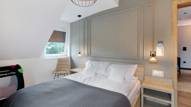 A bedroom with a bed, bedside tables, a chair, a window, and a wall-mounted light fixture.