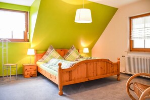 Un dormitorio con techo inclinado, una cama de madera, dos lámparas de noche, un radiador, una ventana con persianas y una silla.