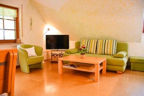 Una sala de estar con un sofá verde, una mesa de centro de madera, un televisor de pantalla plana y una ventana con persianas.
