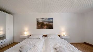 Ein Schlafzimmer mit zwei Betten, einem weißen Kleiderschrank, Nachttischlampen und einem Gemälde einer Strandlandschaft an der Wand.