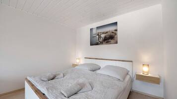 Un dormitorio con una cama, una mesita de noche con lámpara, un estante en la pared y un cuadro sobre la cama.