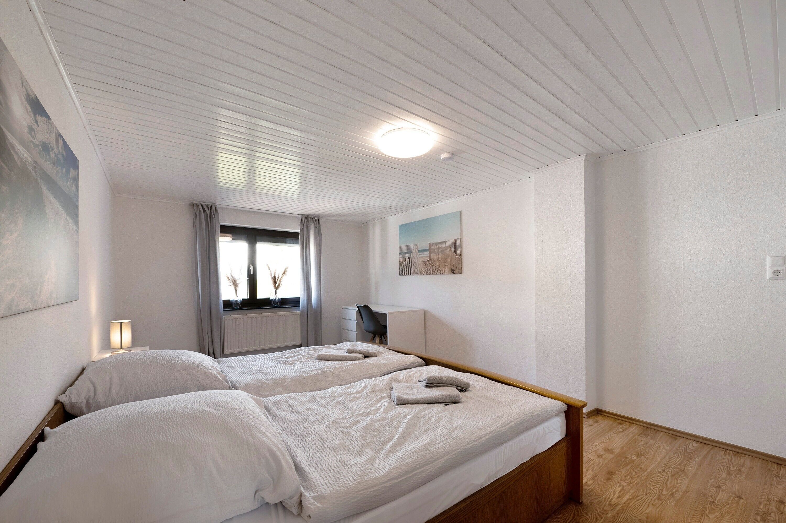 A bedroom with two beds, a window with curtains, a desk, and a radiator.
