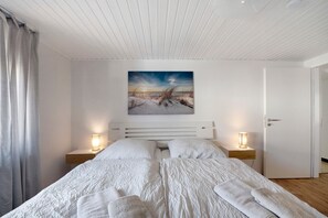 Ein Schlafzimmer mit einem Bett, zwei Nachttischen mit Lampen, einem Gemälde an der Wand und einer Tür rechts.
