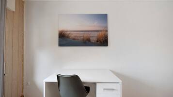 Una habitación con un escritorio blanco, una silla gris y un cuadro de paisaje en la pared.