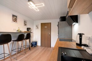 Una cocina moderna con encimera de madera, taburetes negros tipo bar, una cafetera y un hervidor.