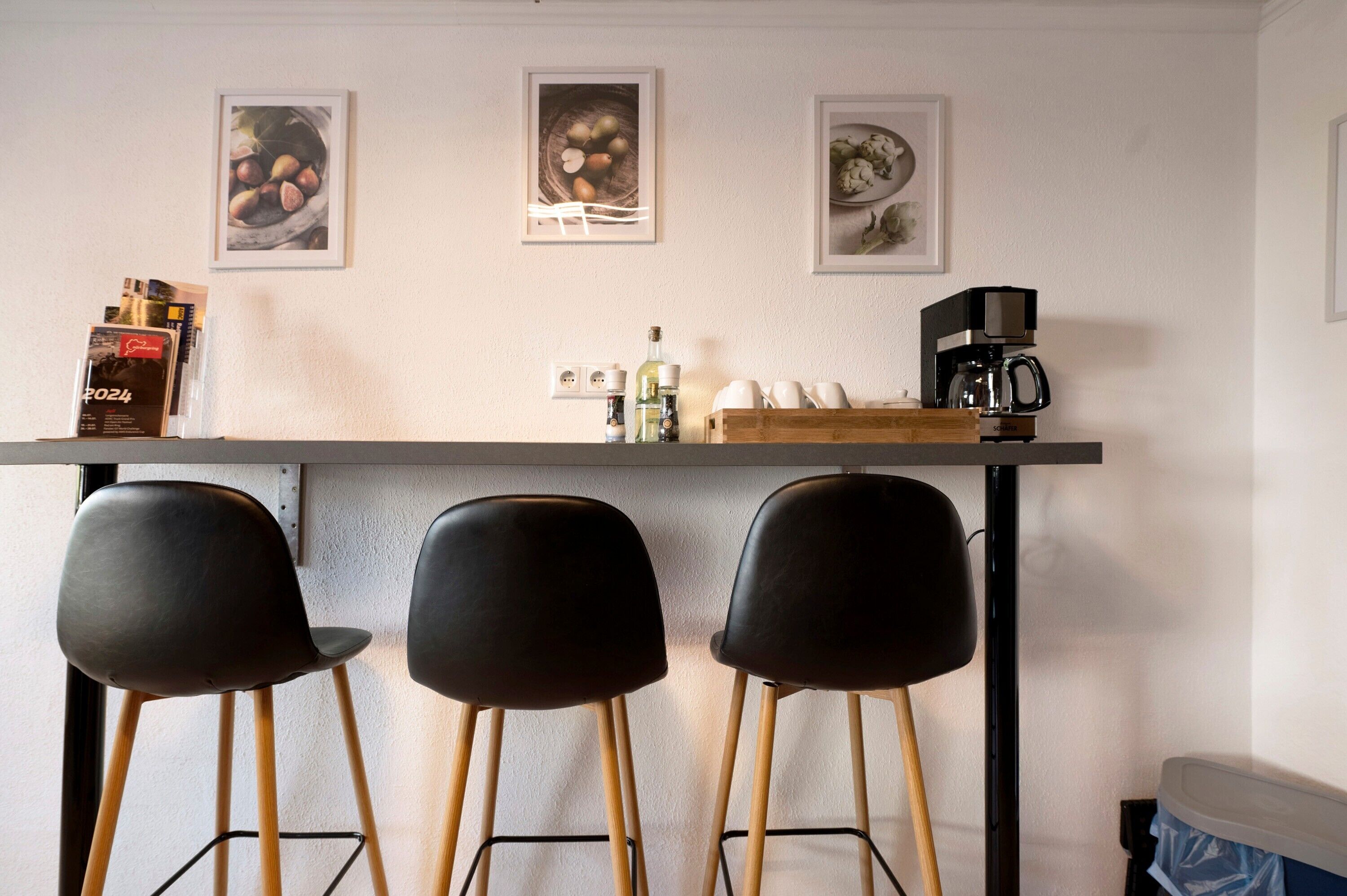 Een bar met drie zwarte stoelen, een koffiemachine en ingelijste foto's aan de muur.