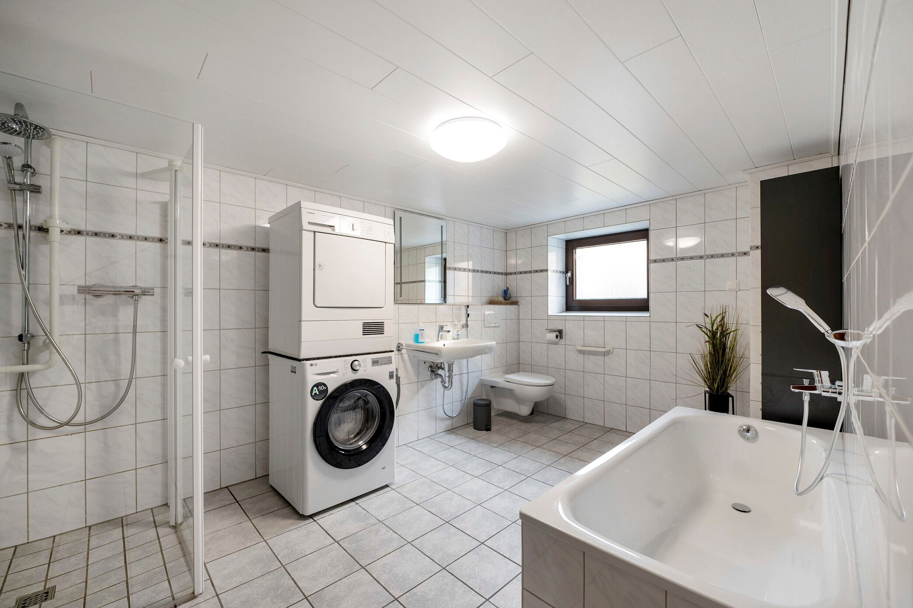 Ett modernt badrum med tvättmaskin, toalett, handfat och badkar.