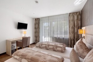 Ett hotellrum med en säng, ett skrivbord, en stol, en tv och ett fönster med gardiner.