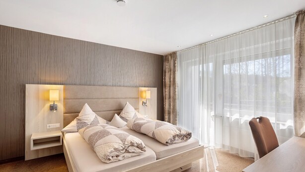 Habitación de hotel moderna con una cama grande, lámparas de noche, un escritorio y vistas al exterior.