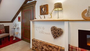 Una habitación con chimenea, repisa de madera, decoración en forma de corazón rojo y un letrero de bienvenida.