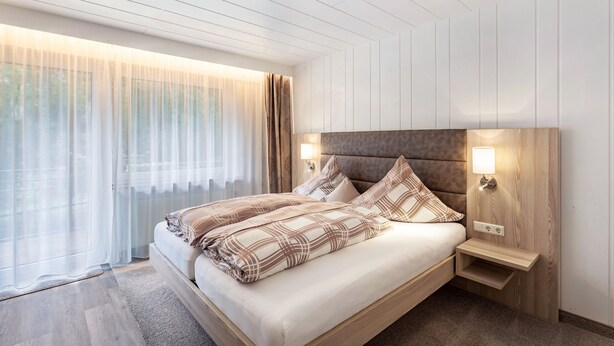 A modern bedroom with a large bed, a headboard, bedside lamps, and a view through sheer curtains. - Apartment 'Typ 2' with Shared Garden, Balcony and Wi-Fi (Willingen (Upland))