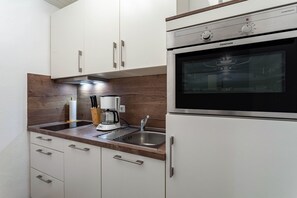 A compact kitchen with white cabinets, a built-in oven, a coffee maker, and a stainless steel sink. - Apartment 'Typ 2' with Shared Garden, Balcony and Wi-Fi (Willingen (Upland))